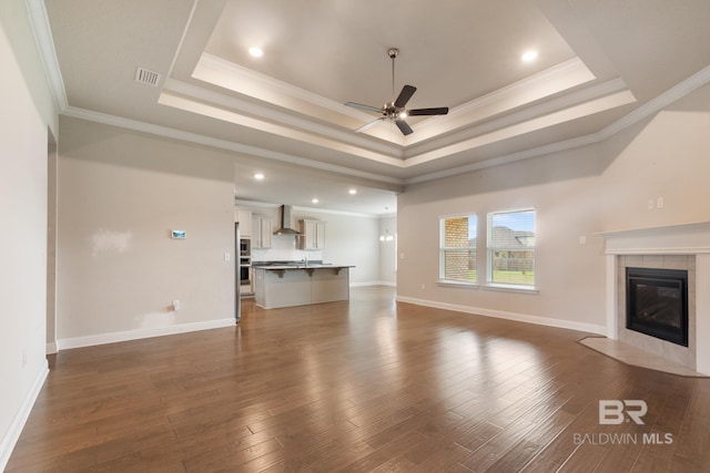 unfurnished living room with ceiling fan, a tiled fireplace, a raised ceiling, and dark wood finished floors