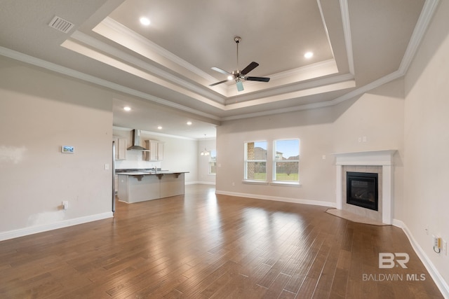 unfurnished living room featuring dark wood-style floors, a tray ceiling, crown molding, a tiled fireplace, and a ceiling fan