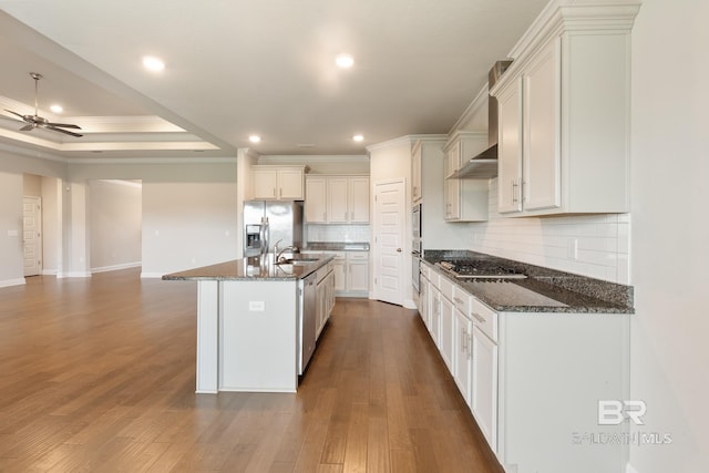 kitchen featuring open floor plan, appliances with stainless steel finishes, dark stone countertops, and a kitchen island with sink