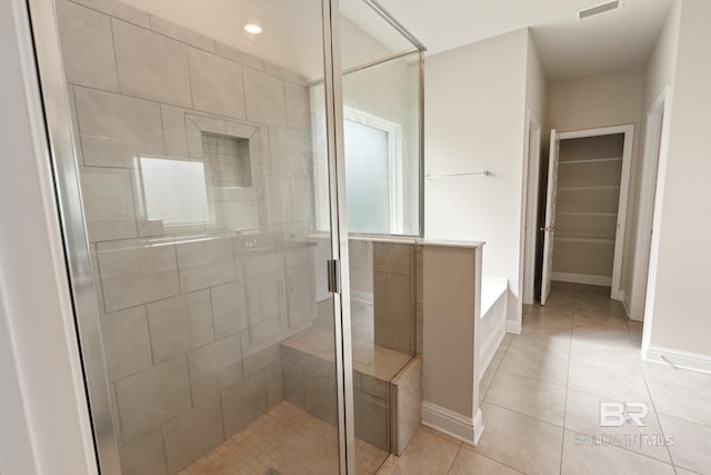 bathroom featuring a walk in closet, a shower stall, baseboards, and tile patterned floors