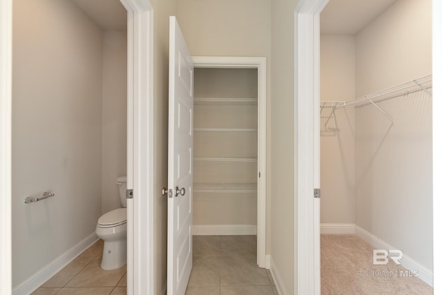 bathroom featuring baseboards, a spacious closet, toilet, and tile patterned floors