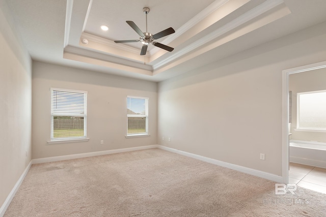 unfurnished room with baseboards, a raised ceiling, light colored carpet, and crown molding