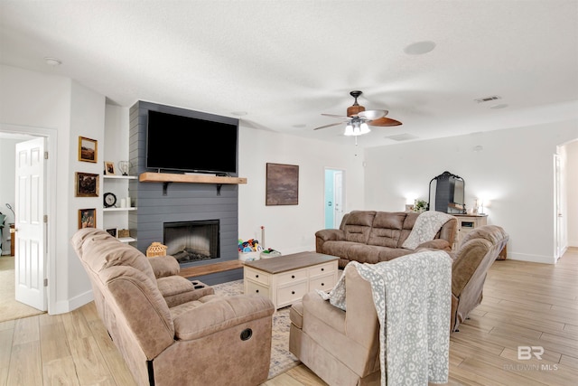 living room with a fireplace, a textured ceiling, light hardwood / wood-style floors, and ceiling fan