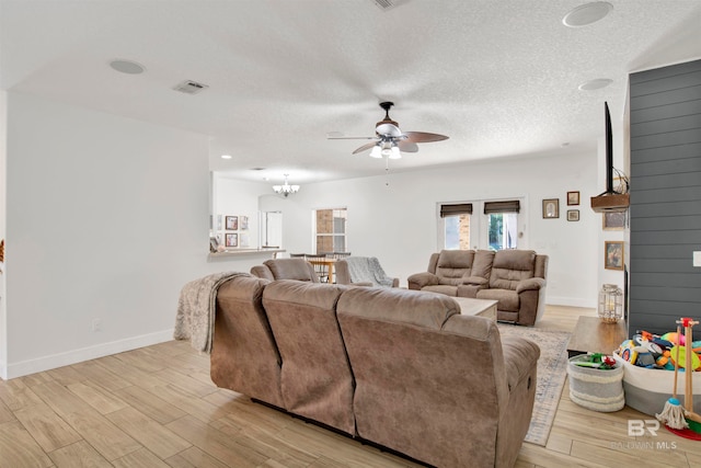 living room featuring ceiling fan with notable chandelier, light wood-type flooring, and a textured ceiling