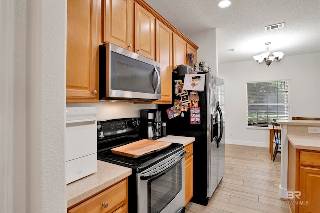 kitchen featuring a chandelier, a textured ceiling, appliances with stainless steel finishes, and light hardwood / wood-style flooring