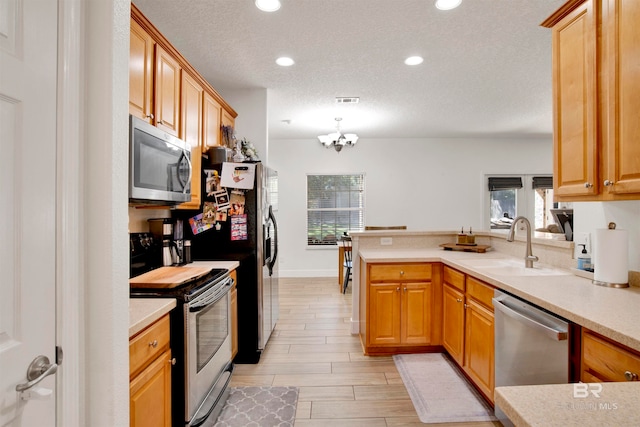 kitchen with pendant lighting, sink, kitchen peninsula, stainless steel appliances, and a chandelier