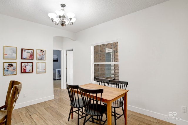 dining room with a textured ceiling, light wood-type flooring, and an inviting chandelier