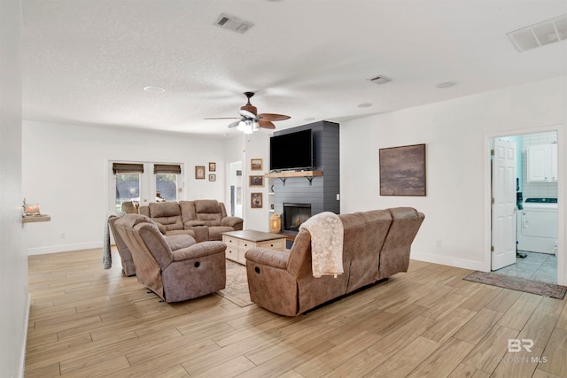 living room with ceiling fan, french doors, light hardwood / wood-style flooring, washer / clothes dryer, and a fireplace