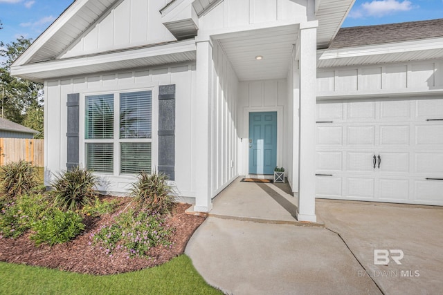 doorway to property featuring board and batten siding, a garage, fence, roof with shingles, and concrete driveway
