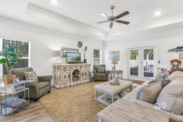 living area featuring crown molding, a tray ceiling, wood finished floors, a ceiling fan, and french doors