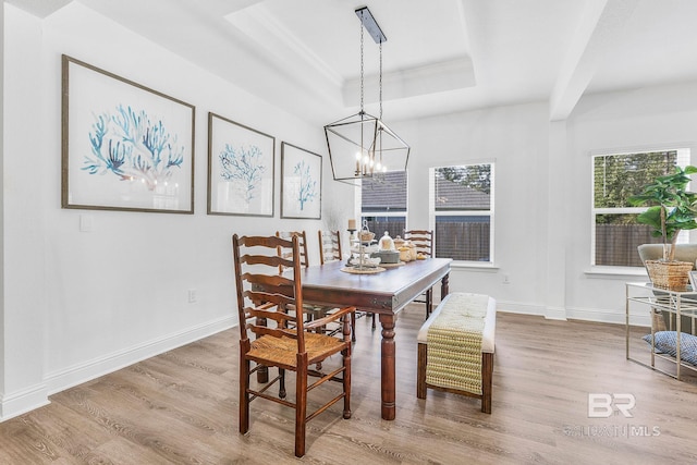 dining area featuring a raised ceiling, wood finished floors, a chandelier, baseboards, and ornamental molding