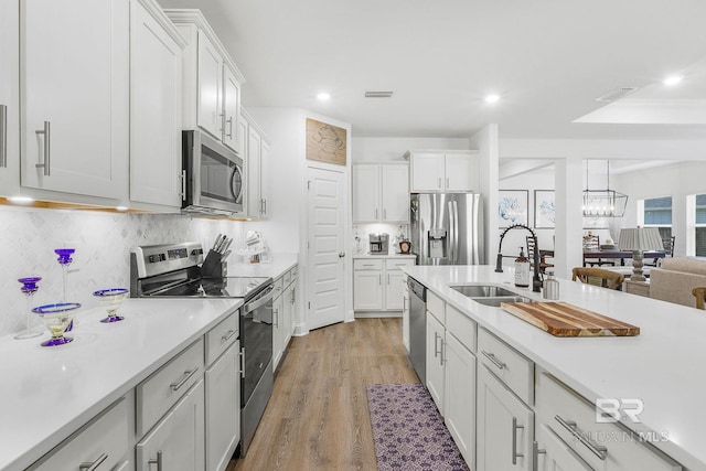 kitchen featuring stainless steel appliances, a sink, light countertops, light wood finished floors, and recessed lighting