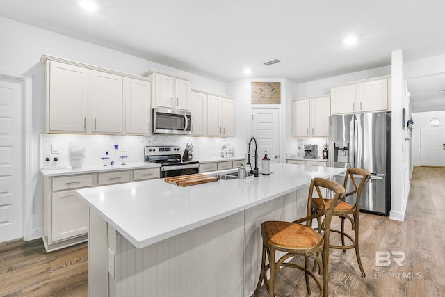 kitchen with stainless steel appliances, a sink, light wood-style floors, a breakfast bar area, and light countertops