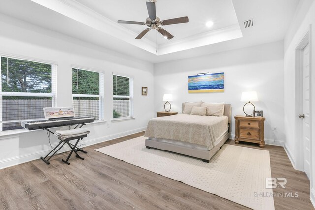 bedroom featuring a raised ceiling, wood finished floors, ornamental molding, baseboards, and recessed lighting