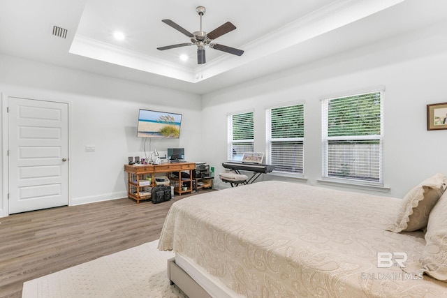 bedroom with wood finished floors, ornamental molding, multiple windows, a tray ceiling, and baseboards