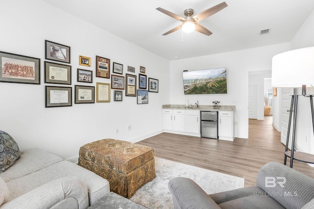 living room with bar with sink, light wood-style flooring, ceiling fan, and baseboards