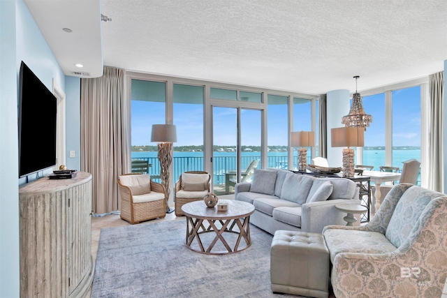 living room featuring an inviting chandelier, a water view, a textured ceiling, and expansive windows