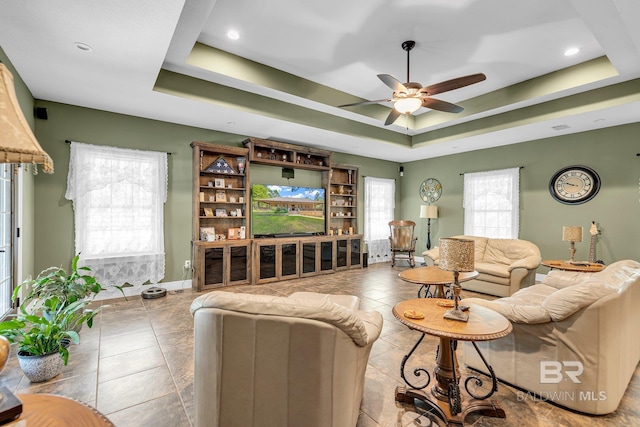 tiled living room featuring ceiling fan and a tray ceiling