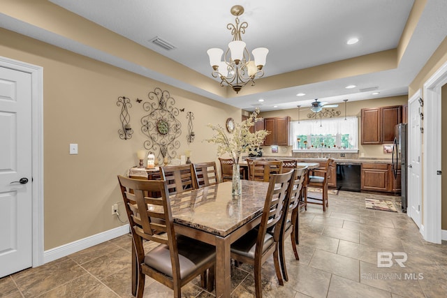 dining area featuring ceiling fan with notable chandelier, sink, and a raised ceiling