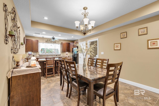 dining space with ceiling fan with notable chandelier and a tray ceiling