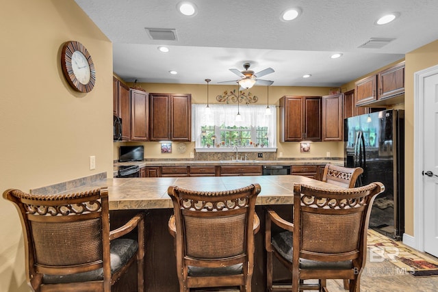 kitchen featuring black appliances, decorative light fixtures, sink, kitchen peninsula, and a breakfast bar