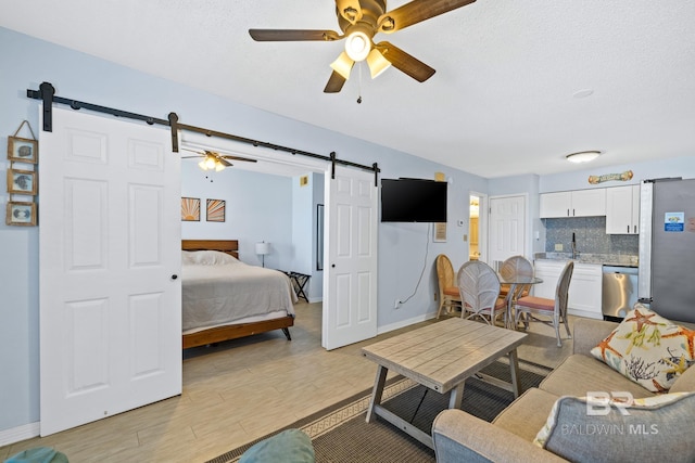 living room with a textured ceiling, ceiling fan, sink, a barn door, and light hardwood / wood-style floors