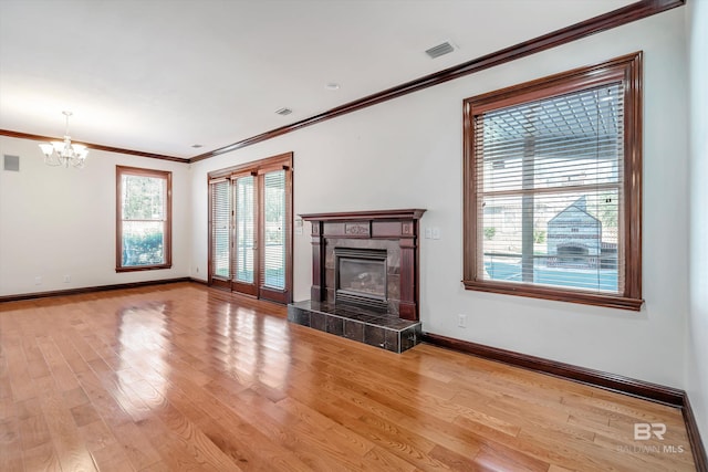 unfurnished living room with light wood-style flooring, a notable chandelier, baseboards, ornamental molding, and a tiled fireplace