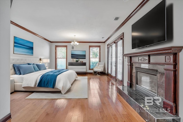 bedroom with a tile fireplace, a notable chandelier, visible vents, light wood finished floors, and crown molding