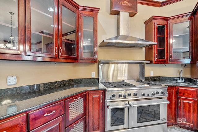 kitchen with range with two ovens, a sink, reddish brown cabinets, wall chimney exhaust hood, and decorative light fixtures