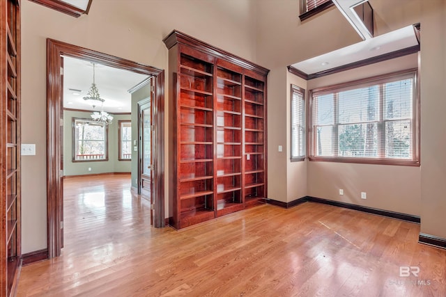 empty room with baseboards, ornamental molding, light wood-type flooring, and a notable chandelier