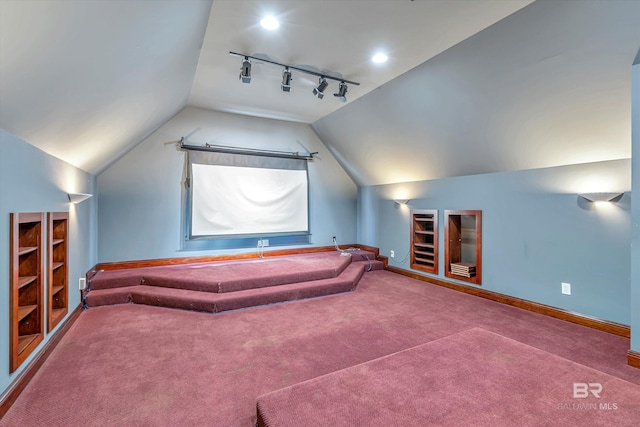 carpeted home theater room with vaulted ceiling, built in shelves, baseboards, and track lighting