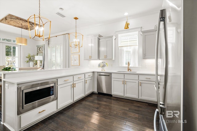 kitchen with kitchen peninsula, stainless steel appliances, sink, decorative light fixtures, and dark hardwood / wood-style floors