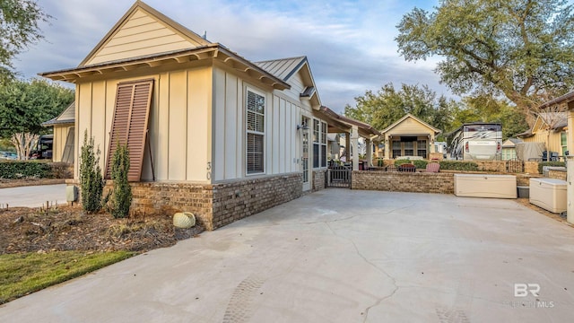 view of side of home featuring metal roof, a standing seam roof, a patio area, board and batten siding, and brick siding