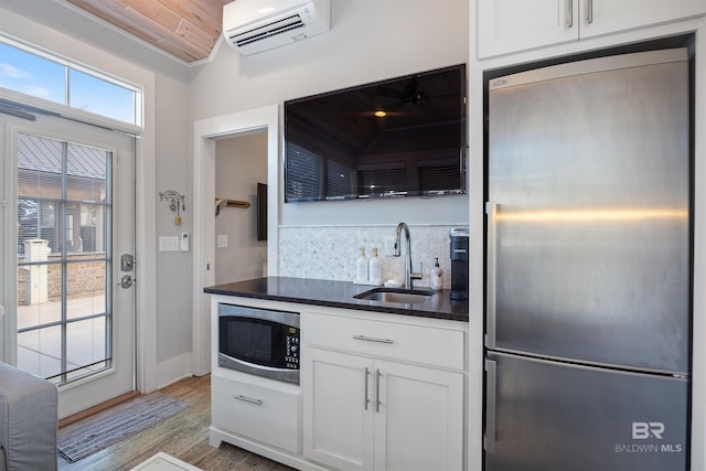 kitchen with dark countertops, stainless steel appliances, an AC wall unit, white cabinetry, and a sink