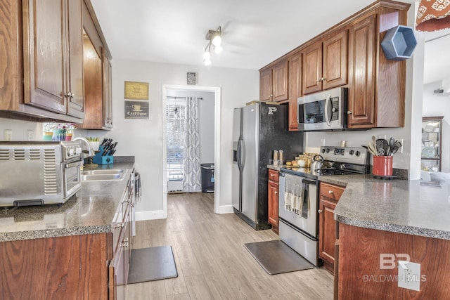 kitchen with stainless steel appliances, light hardwood / wood-style floors, sink, and dark stone counters