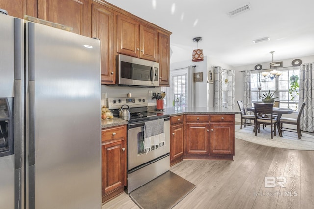 kitchen with pendant lighting, an inviting chandelier, stainless steel appliances, light hardwood / wood-style floors, and kitchen peninsula