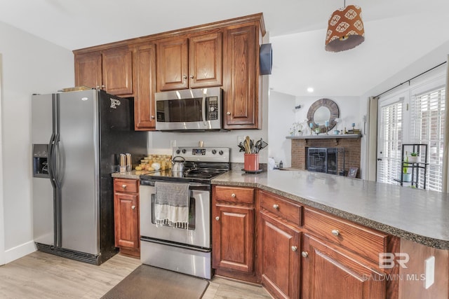 kitchen with stainless steel appliances, a brick fireplace, light hardwood / wood-style floors, and kitchen peninsula