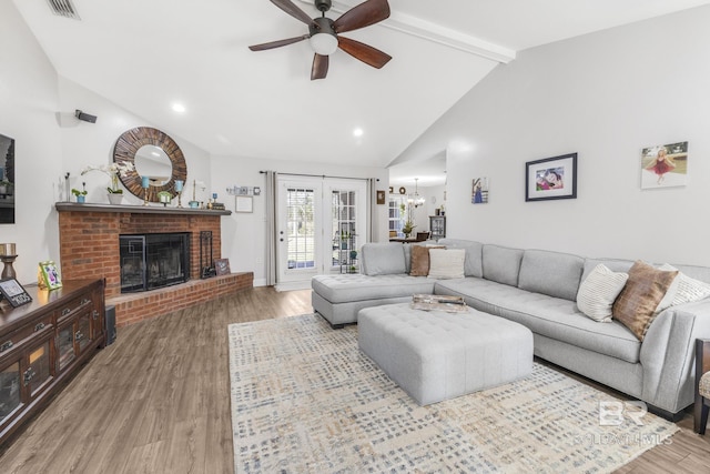 living room with hardwood / wood-style floors, high vaulted ceiling, a fireplace, ceiling fan with notable chandelier, and beamed ceiling