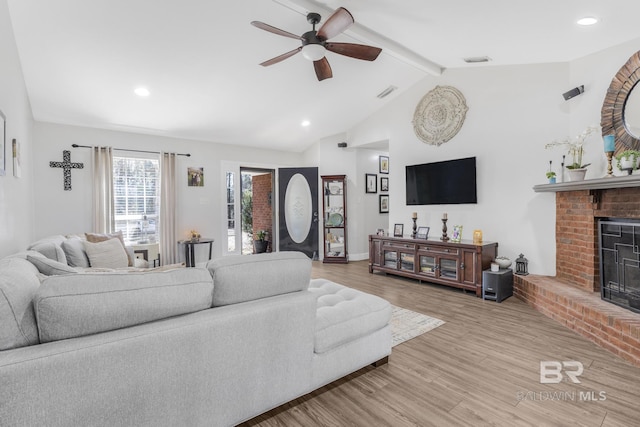 living room featuring ceiling fan, a brick fireplace, lofted ceiling with beams, and light hardwood / wood-style flooring