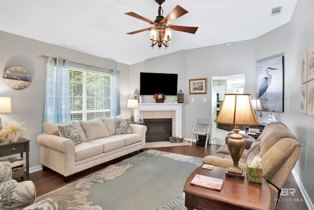 living room featuring wood finished floors, visible vents, baseboards, lofted ceiling, and a tiled fireplace