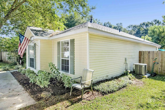 view of side of home featuring central AC unit, a shingled roof, and fence