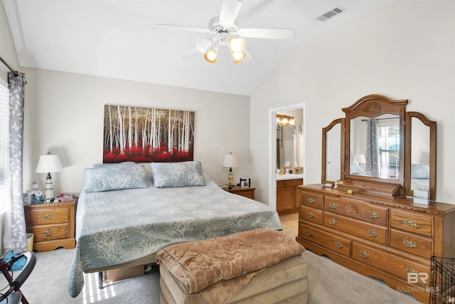 bedroom with visible vents, light colored carpet, vaulted ceiling, ensuite bath, and a ceiling fan