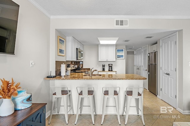 kitchen featuring white cabinets, appliances with stainless steel finishes, kitchen peninsula, light tile patterned flooring, and a breakfast bar