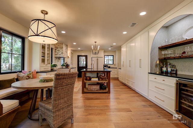 dining area with a notable chandelier, beverage cooler, indoor bar, and light hardwood / wood-style floors