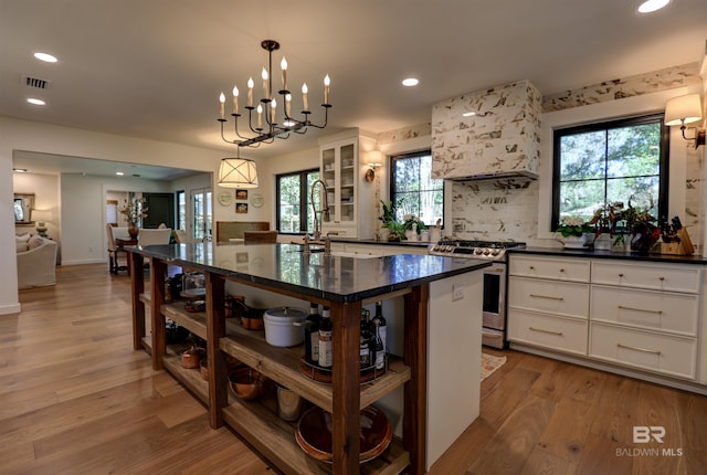 kitchen featuring white cabinets, stainless steel range with gas stovetop, light hardwood / wood-style floors, premium range hood, and a kitchen island