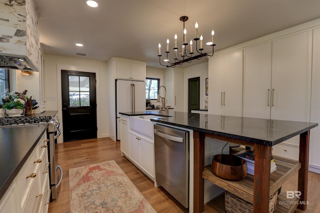 kitchen with an island with sink, stainless steel appliances, white cabinetry, custom exhaust hood, and light wood-type flooring