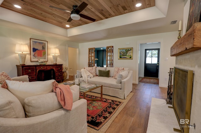 living room featuring a fireplace, ceiling fan, wooden ceiling, hardwood / wood-style flooring, and a tray ceiling