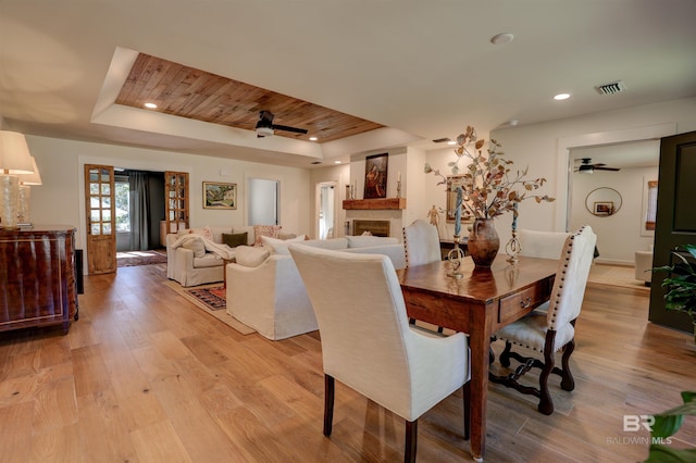 dining space with light wood-type flooring, a raised ceiling, ceiling fan, and wooden ceiling