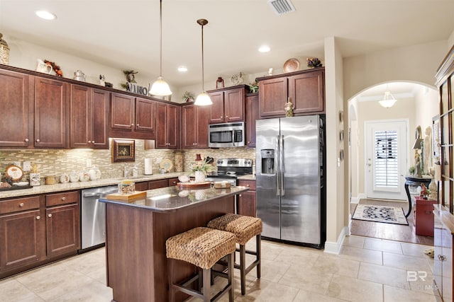 4268 Birkdale St, Gulf Shores, AL 36542 - kitchen featuring stainless steel appliances, arched walkways, tasteful backsplash, a kitchen bar, and light tile patterned flooring