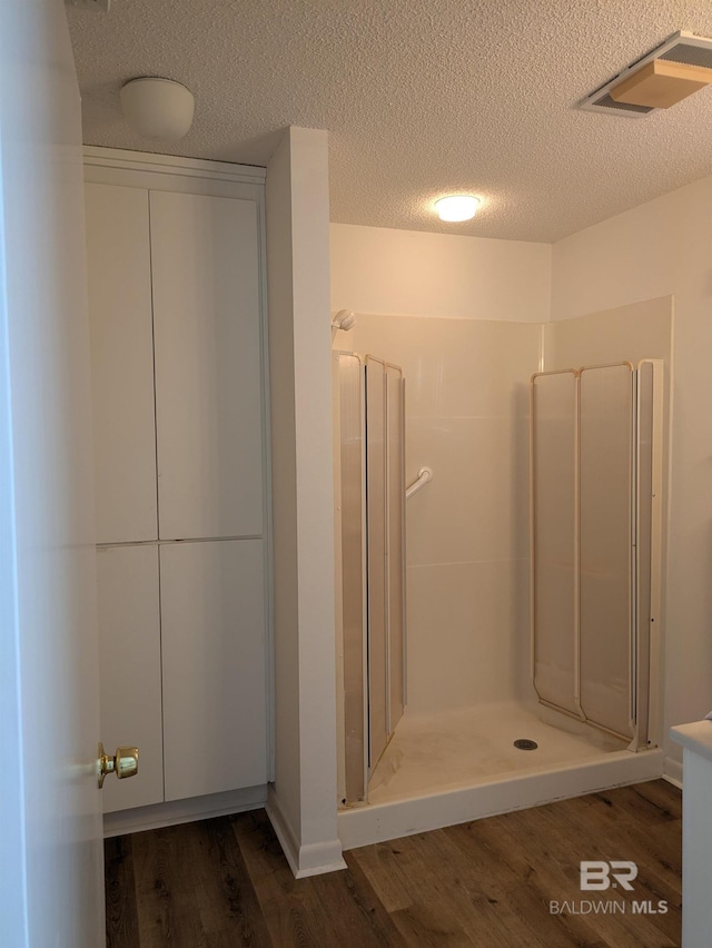bathroom featuring wood finished floors, a textured ceiling, a stall shower, and visible vents